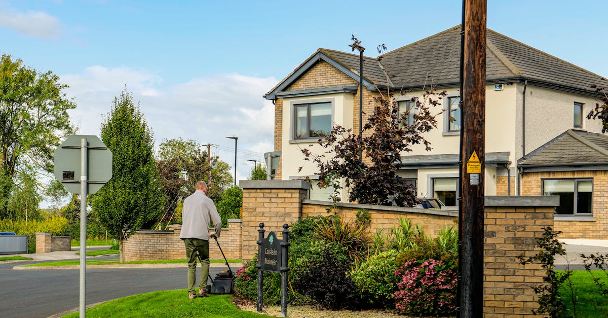 a man mowing the lawn outside a modern suburban home with a lush garden and clear blue sky